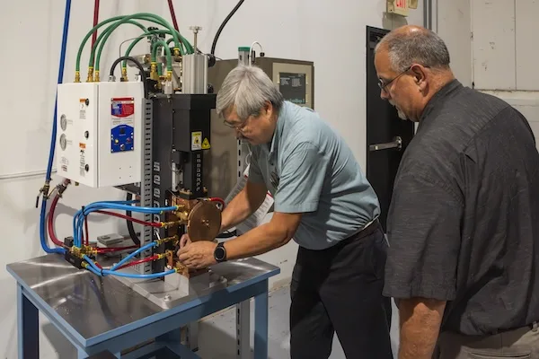 An employee operating a spot welding machine while another employee observes at a slight distance An employee operating a spot welding machine while another employee observes at a slight distance
