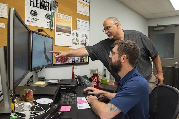 An engineer working in design software while his supervisor points to the screen, discussing the design An engineer working in design software while his supervisor points to the screen, discussing design capabilities